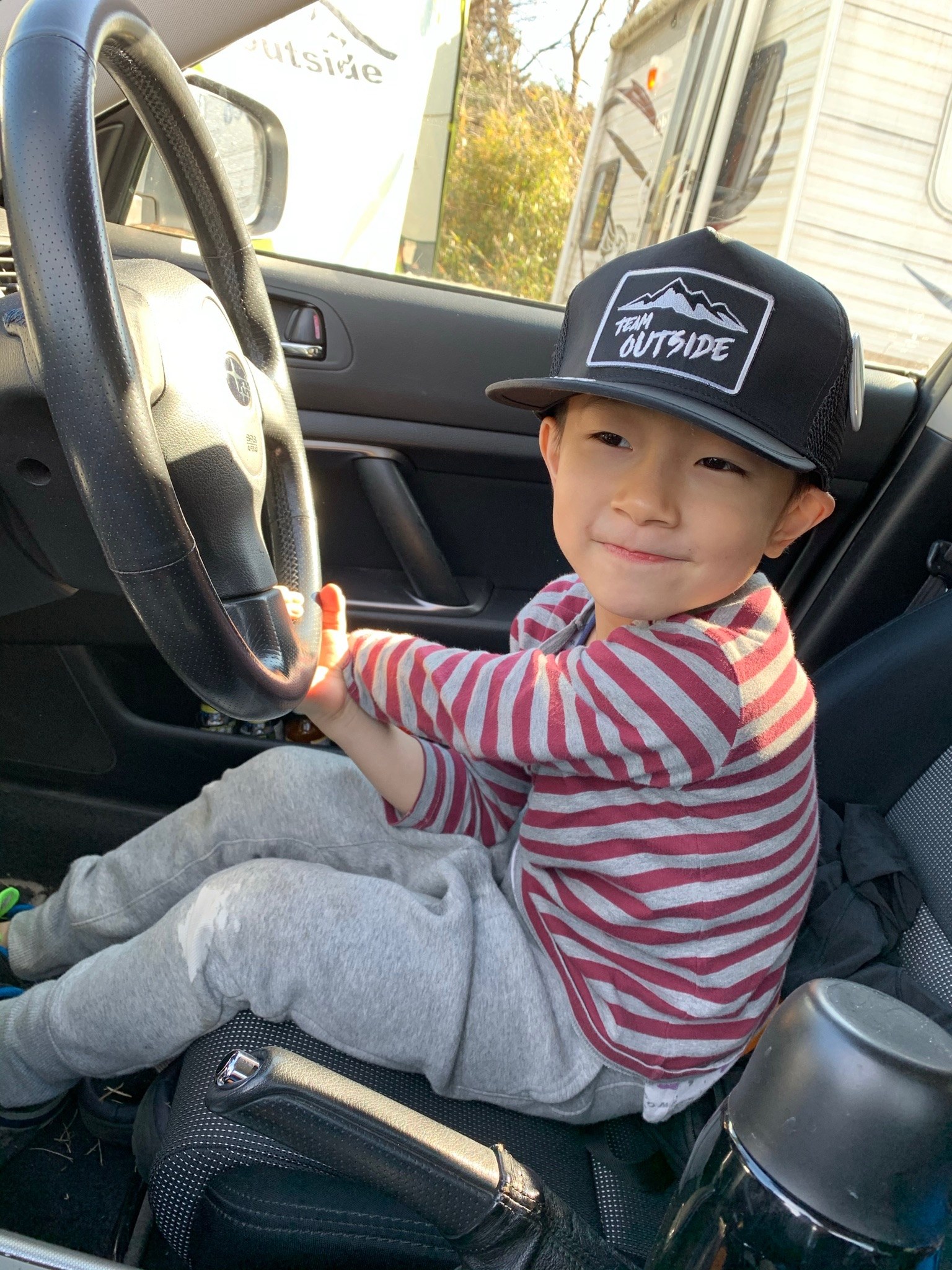 TEAM outsideのキャップをかぶって運転席に座る子ども